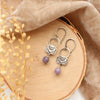The lepidolite jolie earrings styled on wood with tan velvet and dried grass