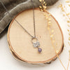 The lepidolite jolie necklace styled on wood with gray velvet and dried grass