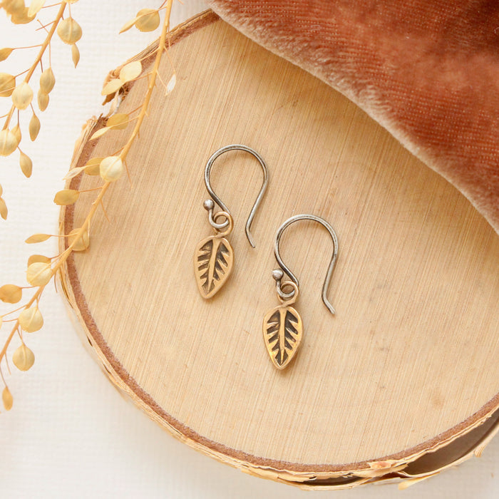 The bronze leaf earrings styled on wood with orange velvet and dried grass