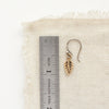 A bronze leaf earring next to a ruler for size reference