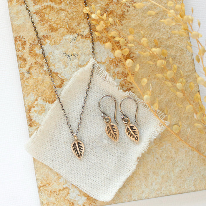 The bronze leaf necklace styled on a tan rock with the matching earrings and linen