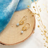 The little aquamarine gold hoop earrings styled on wood with blue velvet and dried grass