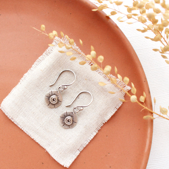 The little musana earrings styled on an orange plate with linen and dried grass