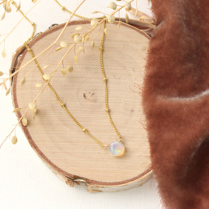 The little opal drop necklace styled on wood with orange velvet and dried grass