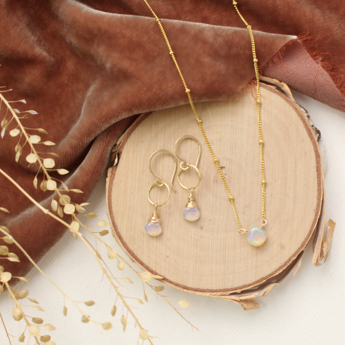 The little opal drop necklace styled on wood with the matching earrings, orange velvet, and dried grass
