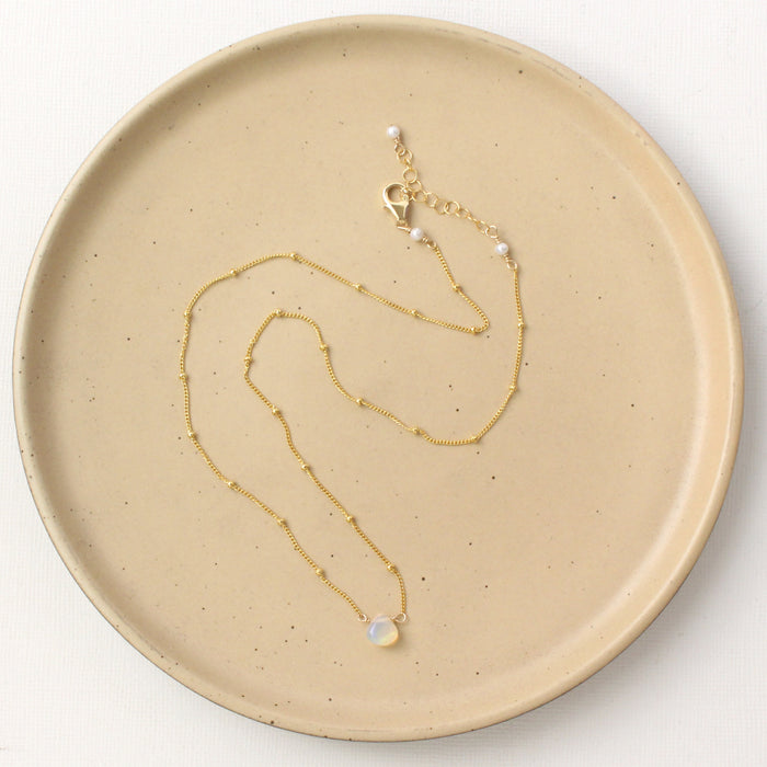 The little opal drop necklace styled on a tan plate to show the adjustable lobster clasp closure