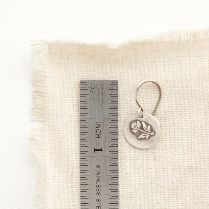 A little rustic rose earring next to a ruler for size reference
