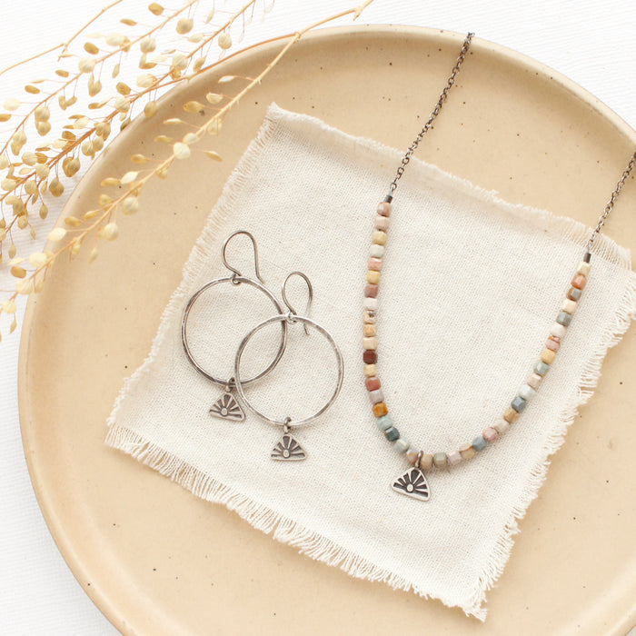 The sun rise hoop earrings styled on a tan plate with the matching necklace
