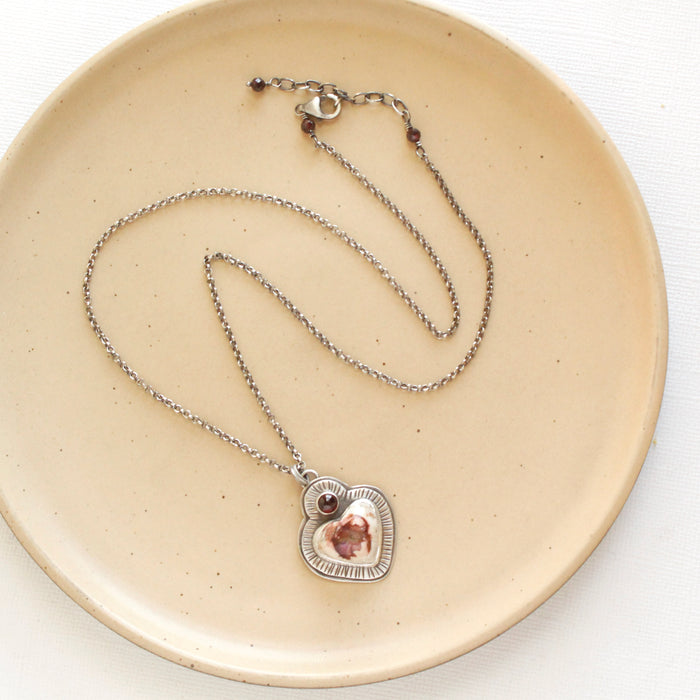 The sacred heart necklace styled on a tan plate to show the adjustable lobster clasp closure
