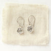 The mini cactus flower charm earrings styled on tan linen