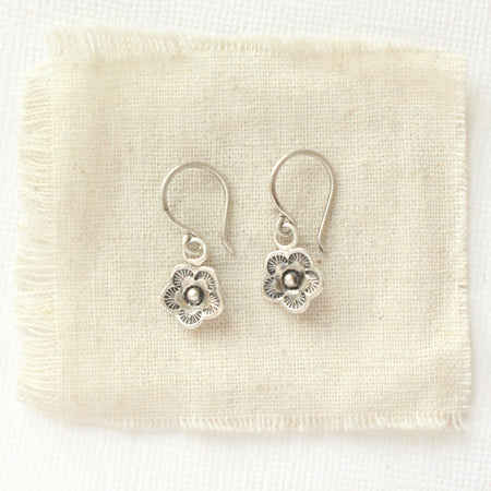 The mini cactus flower charm earrings styled on tan linen