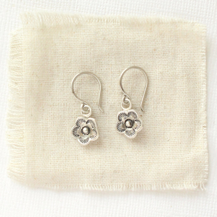 The mini cactus flower charm earrings styled on tan linen