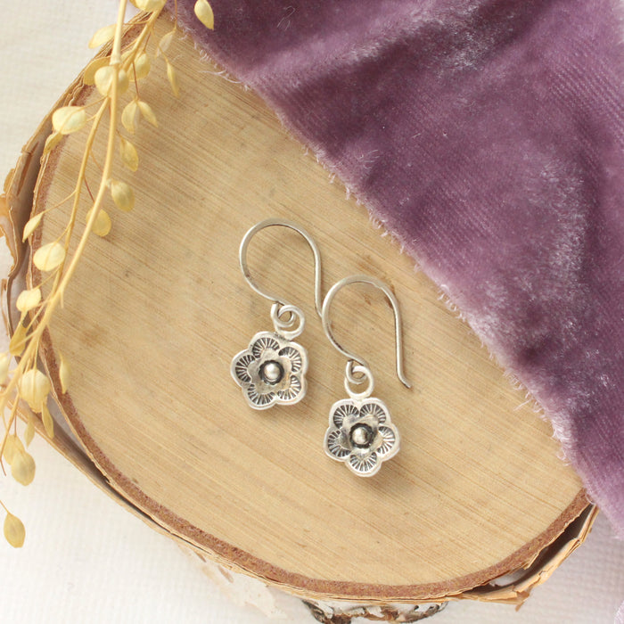 The mini cactus flower charm earrings styled on wood with purple velvet and dried grass