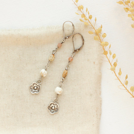 The mini cactus flower long desert earrings style on tan linen with dried grass