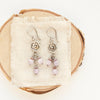 The mini cactus flower lilac dangle earrings styled on tan linen and wood