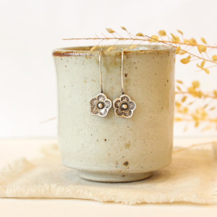 The mini cactus flower lobe hugger earrings styled on a ceramic cup with linen and dried grass