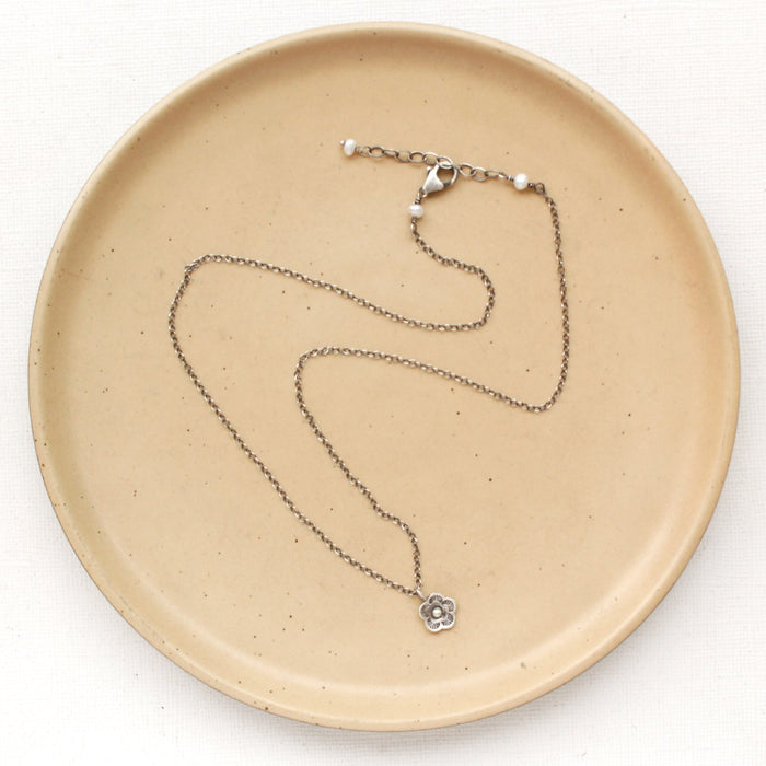 The mini cactus flower necklace styled on a tan plate to show the adjustable lobster clasp closure