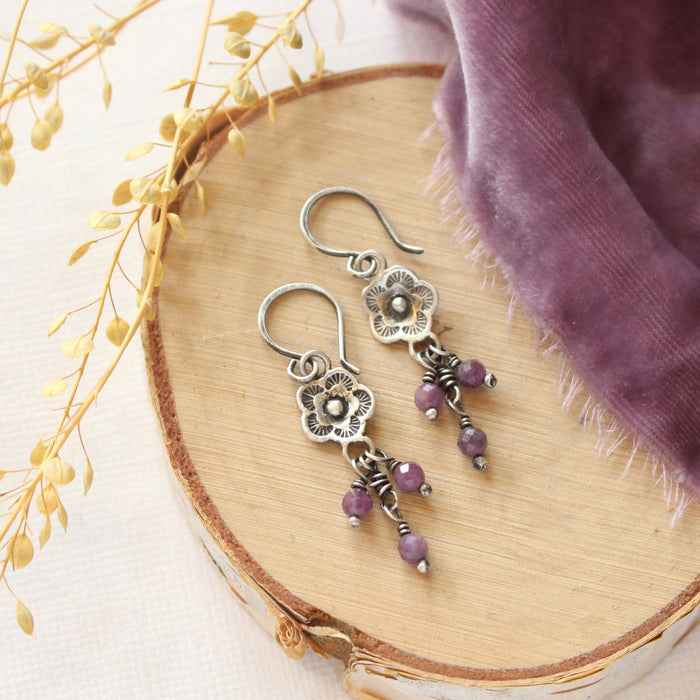 The mini cactus flower purple ruby dangle earrings styled on wood with purple velvet and dried grass