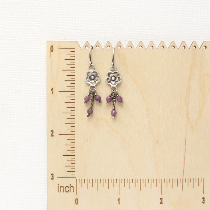 The mini cactus flower purple ruby dangle earrings on a wooden ruler for size reference