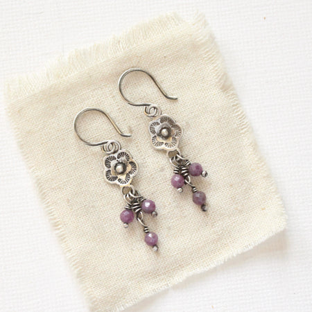The mini cactus flower purple ruby dangle earrings styled on tan linen