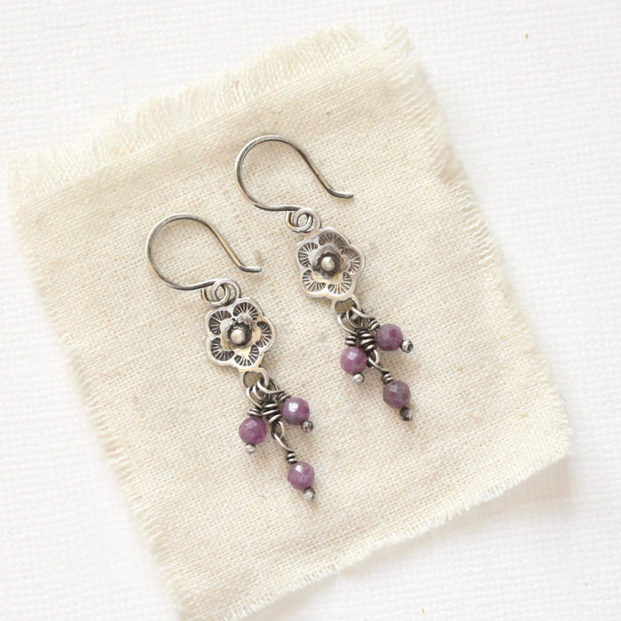 The mini cactus flower purple ruby dangle earrings styled on tan linen