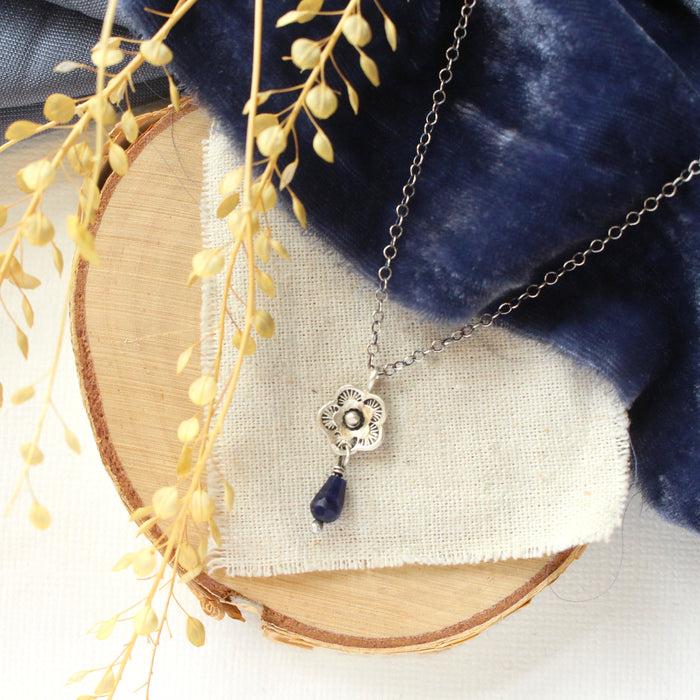 The mini cactus flower sodalite lantern necklace styled on wood with blue velvet, linen, and dried grass
