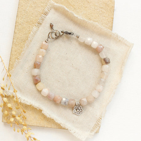 The mini cactus flower violet jade bracelet styled on a tan rock with linen and dried grass