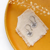 The mini soar earrings styled on a yellow plate with linen and dried grass