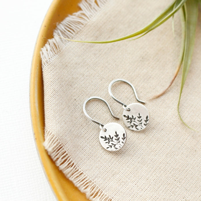 The mini sprout earrings styled on a yellow plate with linen and an airplant