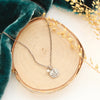 The mini sprout pearl charm necklace styled on wood with blue velvet and dried grass