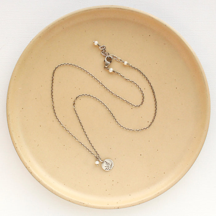 The mini sprout pearl charm necklace styled on a tan plate to show the adjustable lobster clasp closure