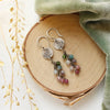 The mini sprout rainbow tourmaline earrings styled on wood with green velvet and dried grass