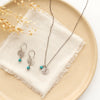 The mini sprout turquoise dangle earrings styled on a tan plate with the matching necklace