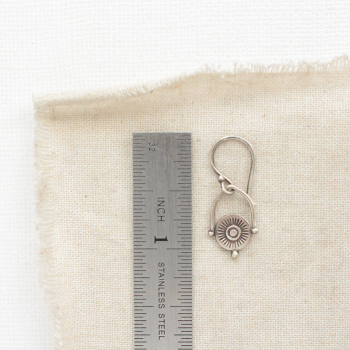 A mini talara shield earring next to a ruler for size reference