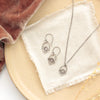 The mini talara shield earrings styled on a tan plate with the matching necklace, linen, orange velvet, and dried grass