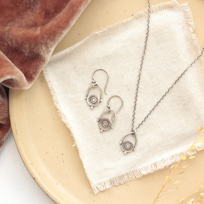 The mini talara shield earrings styled on a tan plate with the matching necklace, linen, orange velvet, and dried grass