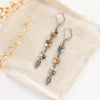 The long mixed gemstone leaf earrings styled on tan linen with dried grass