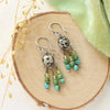 The monica chandelier earrings styled on wood with green velvet and dried grass