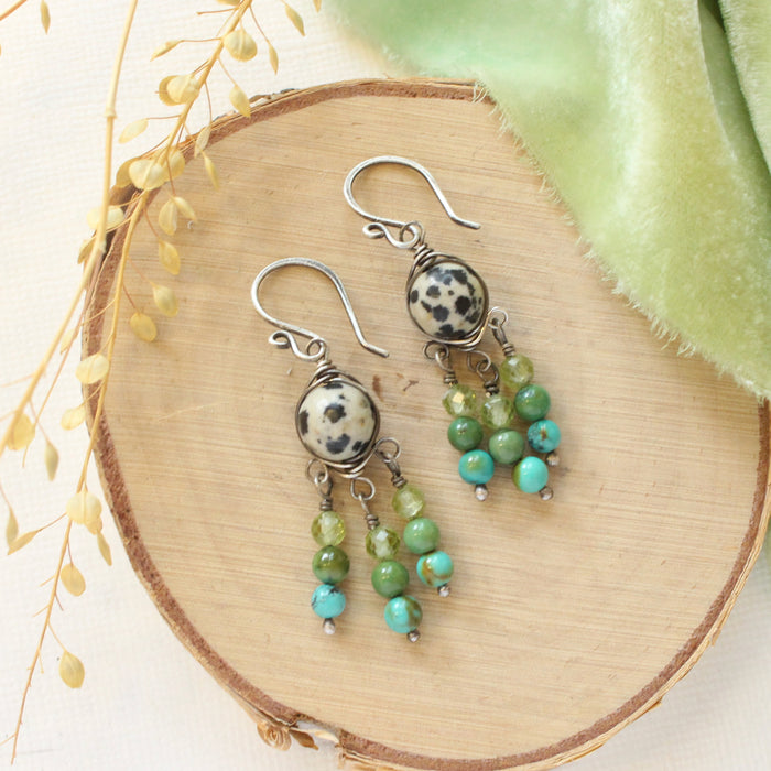 The monica chandelier earrings styled on wood with green velvet and dried grass