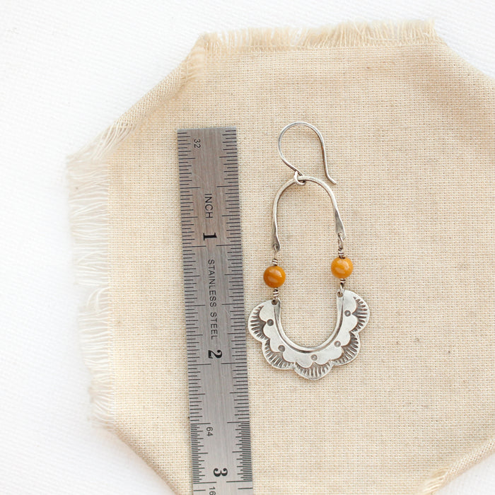 A mookaite columbine hoop earring next to a ruler for size reference