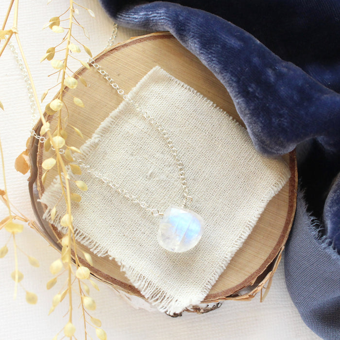 The silver moonstone drop necklace styled on wood with blue velvet and dried grass