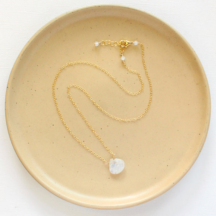 The gold moonstone drop necklace styled on a tan plate to show the adjustable lobster clasp closure