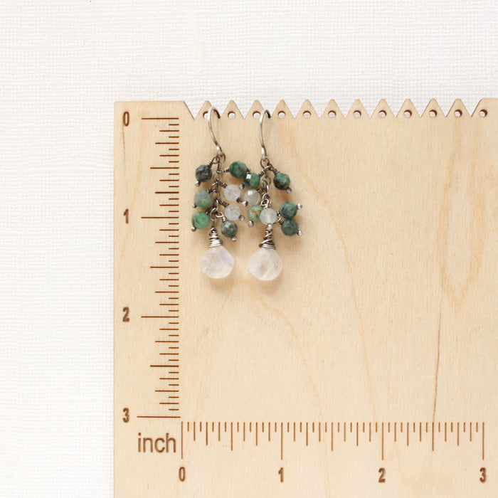 The moonstone and emerald fringe earrings on a wooden ruler for size reference