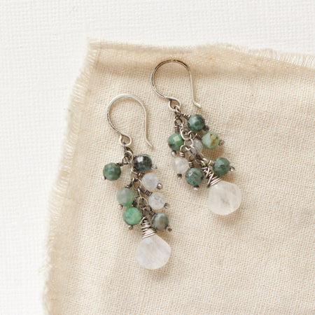 The moonstone and emerald fringe earrings styled on tan linen