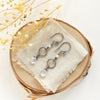 The moonstone and pearl hoop earrings styled on wood with linen and dried grass
