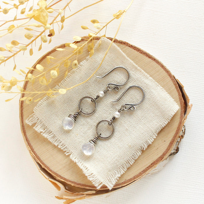 The moonstone and pearl hoop earrings styled on wood with linen and dried grass