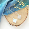 The moonstone slice petal earrings styled on wood with blue velvet and dried grass