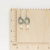 The mother of pearl and aquamarine hoop earrings styled on a wooden ruler