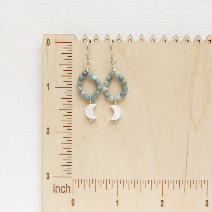 The mother of pearl and aquamarine hoop earrings styled on a wooden ruler