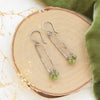The olivine jade wrapped forged long hoop earrings styled on wood with green velvet and dried grass